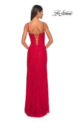 A woman models the La Femme Lace-Up Back Long Lace Prom Dress 32237, a red lace designer gown with thin straps, a corset-style bodice, and lace-up back detail, standing facing away from the camera.