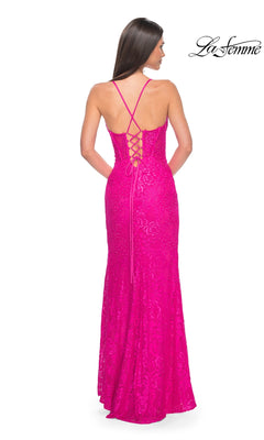 A woman stands facing away, wearing the La Femme Floral-Lace Long Corset Prom Dress 32248 in bright pink, featuring crisscrossed straps, a lace-up back, and a corset-style bodice.