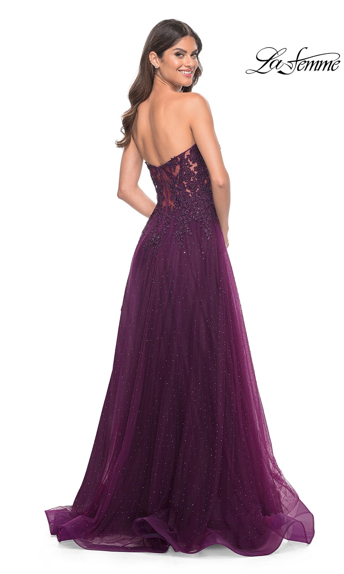 A woman in the La Femme Sheer-Lace Long Beaded Prom Dress 32253—a floor-length, purple strapless gown with lace and sequin accents—smiles as she faces backward against a white background.