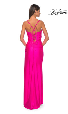 Woman in a bright pink La Femme Long Bustier-Bodice Prom Dress 32256, featuring crisscross straps, corset-style bodice, and lace-up back, stands facing away from the camera. "La Femme" logo appears in the top right corner.