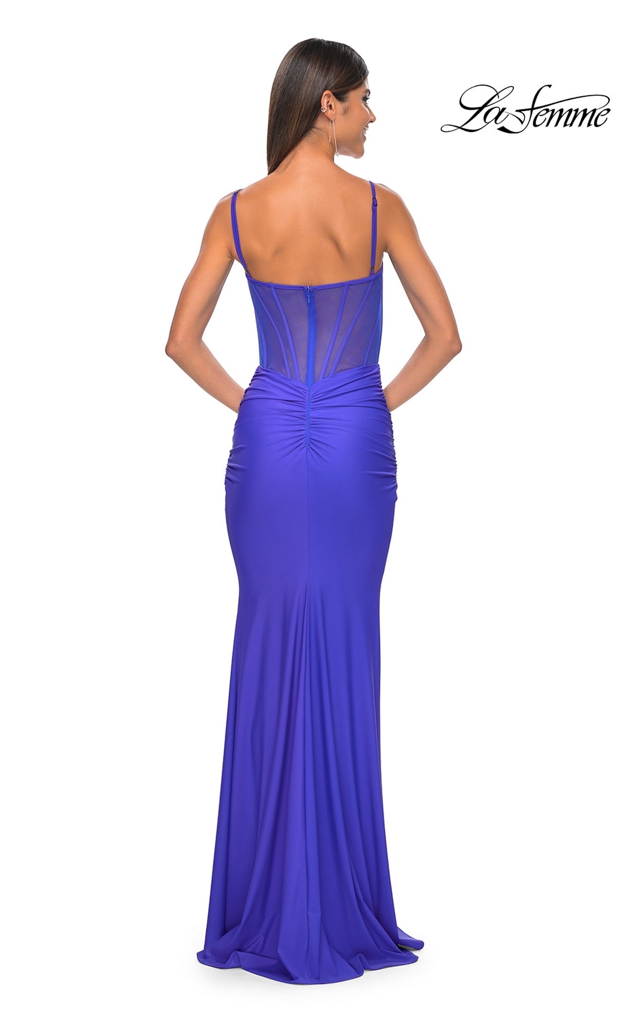 A woman models the La Femme Sheer-Back Long Corset Prom Dress 32257 in royal blue, featuring spaghetti straps, a sheer-back panel, and ruched detailing; this elegant floor-length gown is shown from behind.
