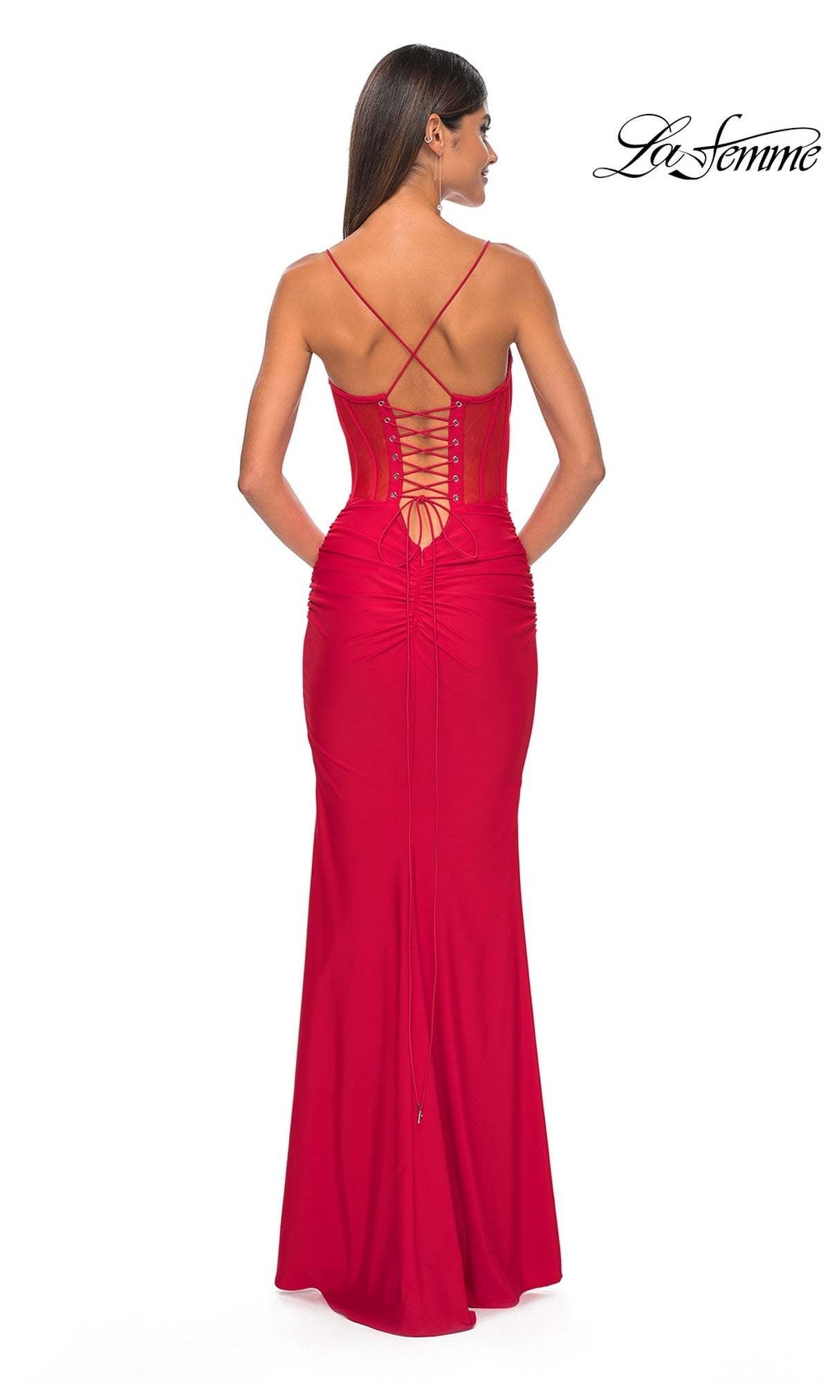 Woman wearing the La Femme Sheer-Corset Long Prom Dress 32258 in red, featuring crisscross straps and a lace-up corset back, stands with her back to the camera. The 