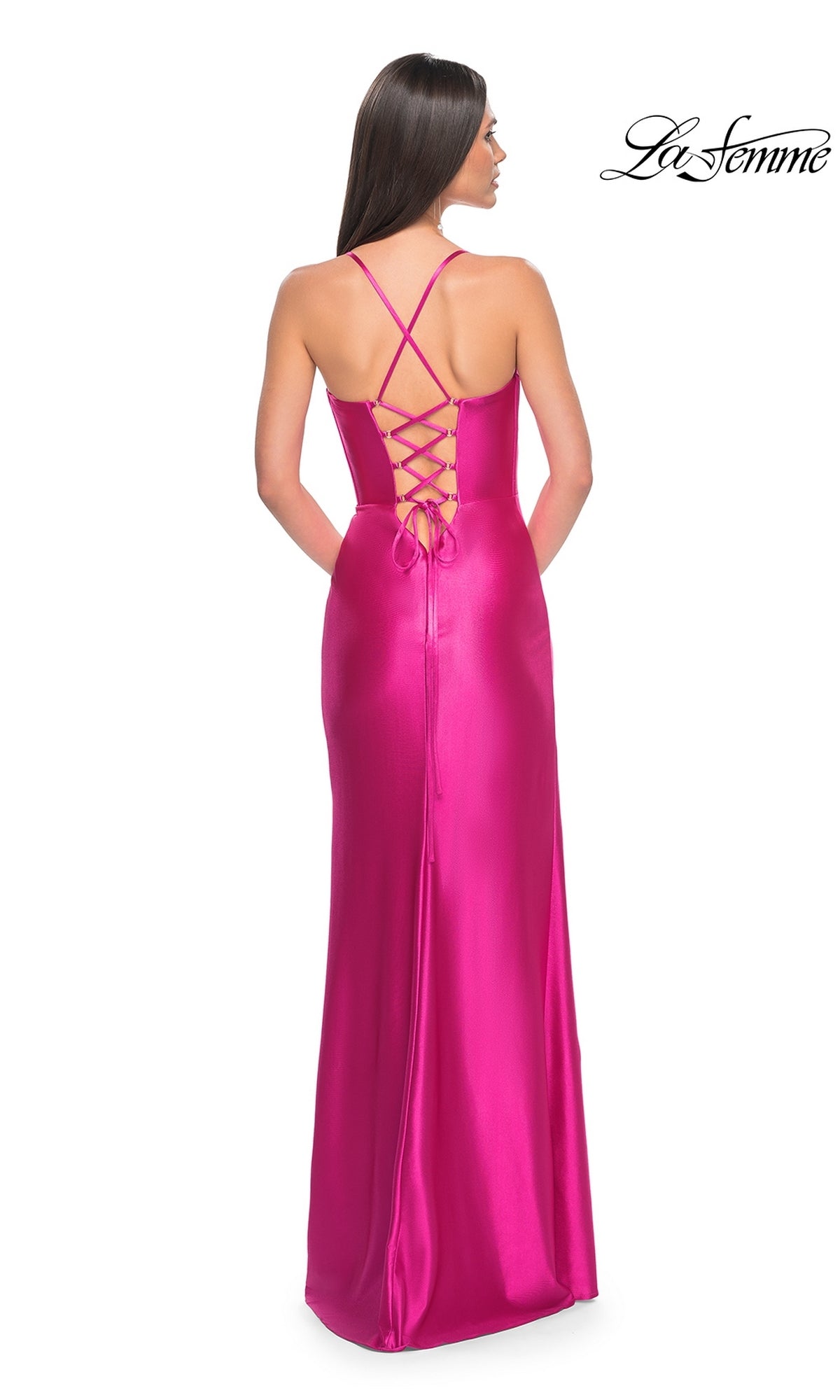 A woman faces away, wearing the La Femme Bright Neon Long Prom Dress 32262—floor-length fuchsia satin with a corset bodice, lace-up back, and thin crisscross straps. The 