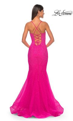 A woman faces away from the camera in the La Femme Embellished Long Mermaid Prom Dress 32273, a bright pink floor-length gown with a lace-up open back and thin crisscross straps.