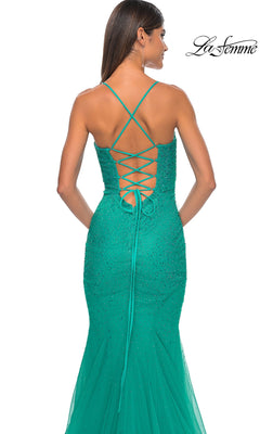 A woman wears the La Femme Embellished Long Mermaid Prom Dress 32273—a fitted green beaded gown featuring a lace-up open back and thin crisscross straps. The La Femme logo appears in the top right corner.