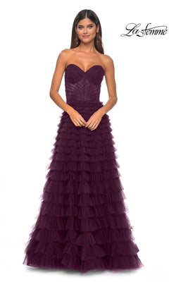 A woman wears the La Femme Strapless Long Ruffled Prom Dress 32283 in dark purple, featuring layered tulle, as she stands against a white background.