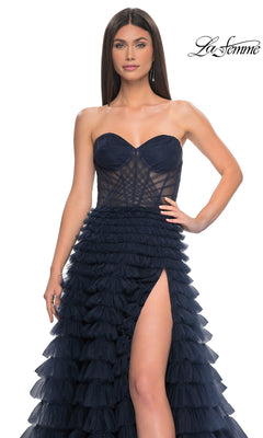 A woman wears the La Femme Strapless Long Ruffled Prom Dress 32283 in navy blue, featuring a sheer bodice, high thigh slit, and layered ruffled A-line skirt. The "La Femme" logo appears in the top right corner.