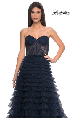 A woman wears the La Femme Strapless Long Ruffled Prom Dress 32283, a navy blue tulle gown with a strapless, fitted sheer bodice and ruffled A-line details. The La Femme logo appears in the top right corner.