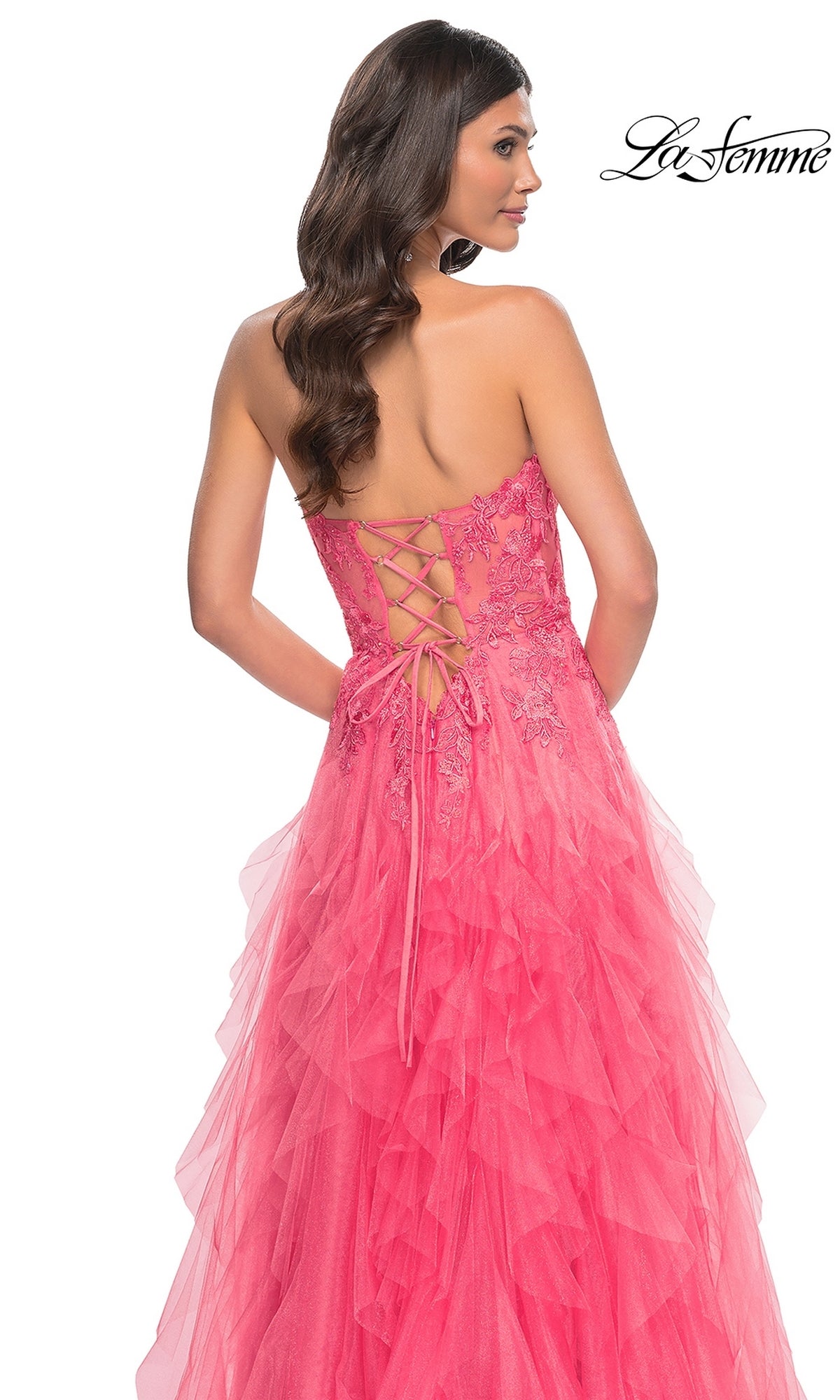 A woman, seen from behind, wears the La Femme Strapless Long Coral Prom Dress 32286 featuring a beaded-lace bodice and layered tulle skirt. The 