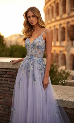 A woman in the La Femme Long Lavender A-Line Prom Dress 32288 with floral embroidery stands by a stone wall as the Colosseum glows at sunset behind her.