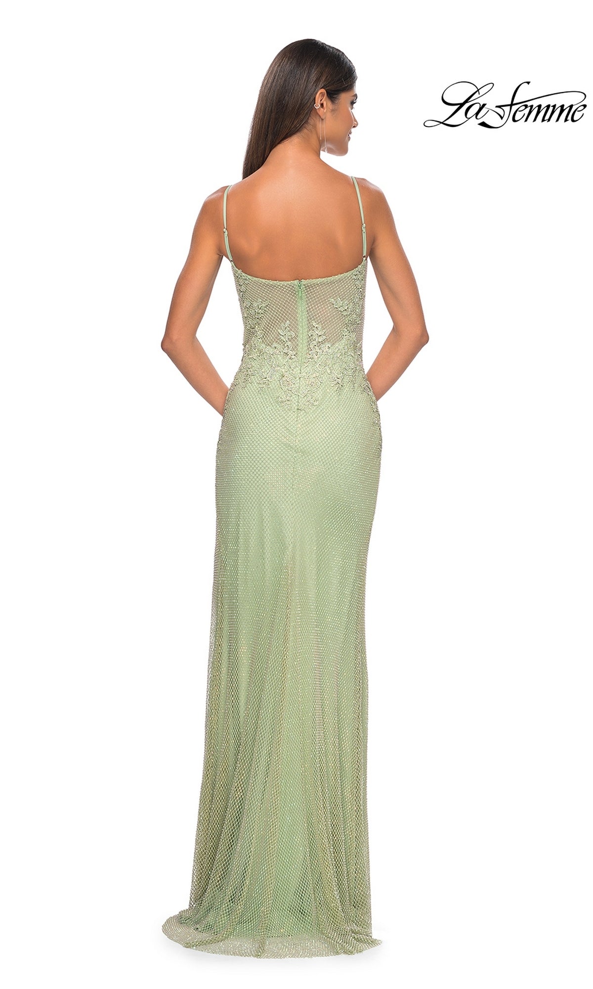 A woman is elegantly shown from the back in the La Femme Embellished Long Fishnet Prom Dress 32292, a light green, floor-length gown with thin straps, intricate lace beading, and a corset-style bodice.