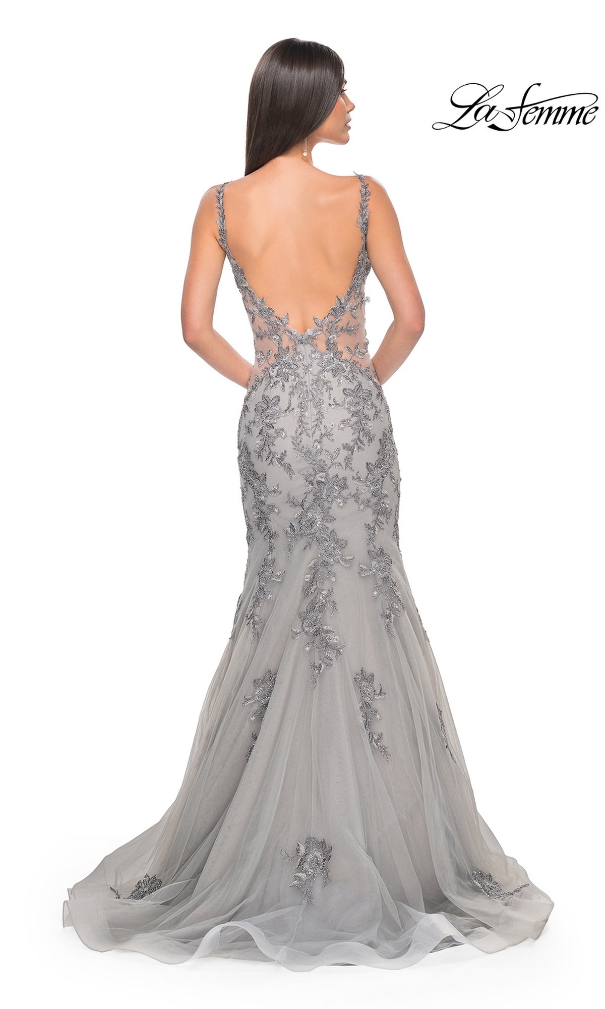 A woman faces away, wearing the La Femme Backless Long Mermaid Prom Dress 32295 in gray with lace applique and a floor-length backless design. The 