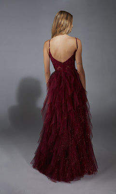 A person with long blonde hair wears the Aerie Couture 322 Glitter Ruffle Prom Ball Gown—deep red, glittery, thin straps, tiered skirt with leg slit—shown from the back against a gray background.