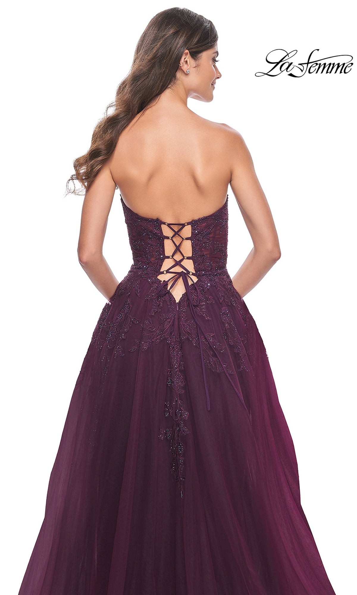 A woman wearing the La Femme Lace-Up Long Sweetheart Prom Dress 32304 in deep purple, featuring a strapless design, embroidered detailing, and a lace-up back, is shown from behind.