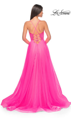 A woman in the La Femme Lace-Bodice Long A-Line Prom Dress 32306, a bright pink gown with a lace-up back, crisscross straps, and a flowing sheer floor-length skirt for an elegant statement.