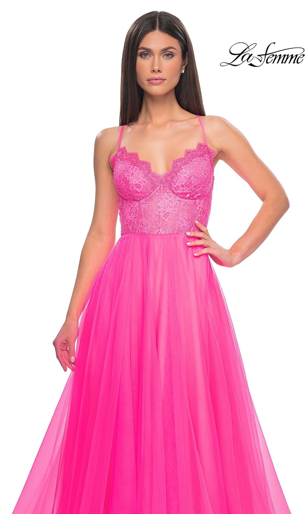 A woman in the La Femme Lace-Bodice Long A-Line Prom Dress 32306, a bright pink gown with lace and tulle, thin straps, a fitted bodice, and flowing skirt, stands against a white background.