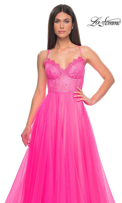A woman in the La Femme Lace-Bodice Long A-Line Prom Dress 32306, a bright pink gown with lace and tulle, thin straps, a fitted bodice, and flowing skirt, stands against a white background.