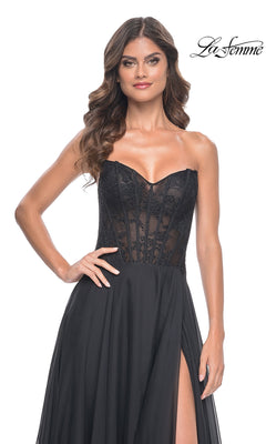 A woman stands against a white background wearing the La Femme Sheer-Waist Long A-Line Prom Dress 32313, featuring a strapless black design with a beaded lace bodice, sheer corset-style waist, and high slit.