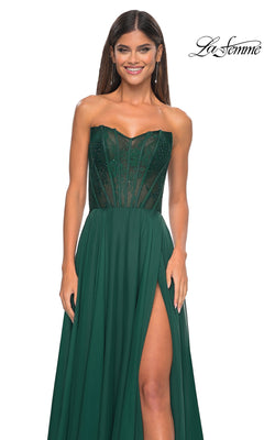Smiling woman in the La Femme Lace-Bodice Long A-Line Prom Dress 32311, featuring a strapless emerald green sheer corset bodice, high slit, and flowing skirt, stands against a white background.
