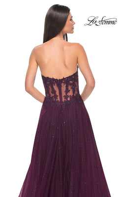 Woman in the La Femme Sheer-Waist Long A-Line Prom Dress 32313, a strapless deep purple gown with a shimmer overlay, beaded lace bodice, and sheer lace back, standing against a white background.