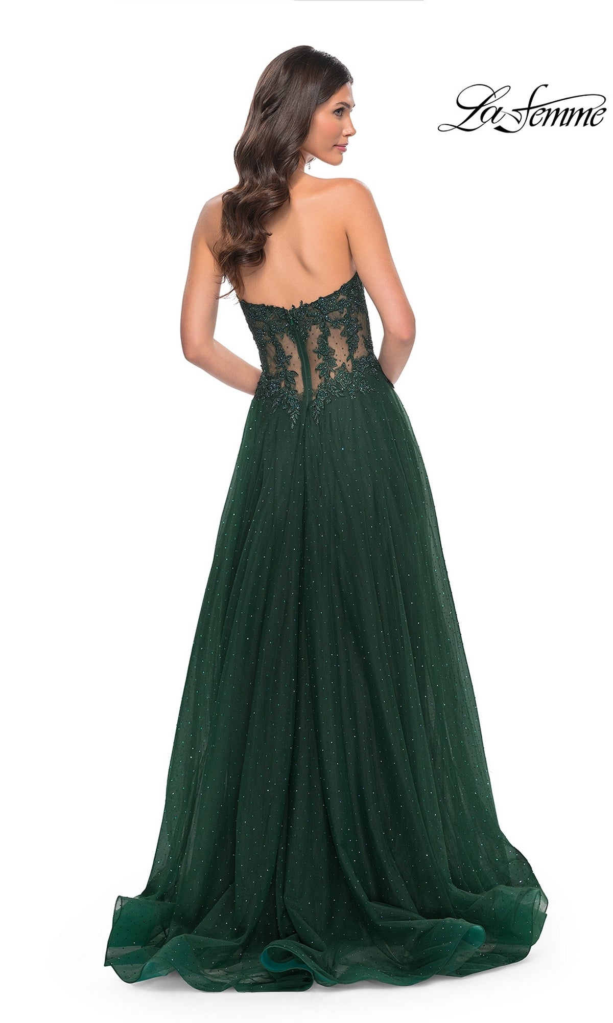 A woman stands with her back to the camera in the La Femme Sheer-Waist Long A-Line Prom Dress 32313, featuring a strapless dark green design with a sheer beaded lace bodice and flowing skirt. The 