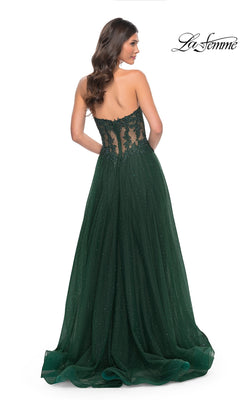 A woman stands with her back to the camera in the La Femme Sheer-Waist Long A-Line Prom Dress 32313, featuring a strapless dark green design with a sheer beaded lace bodice and flowing skirt. The "La Femme" logo appears in the top right corner.