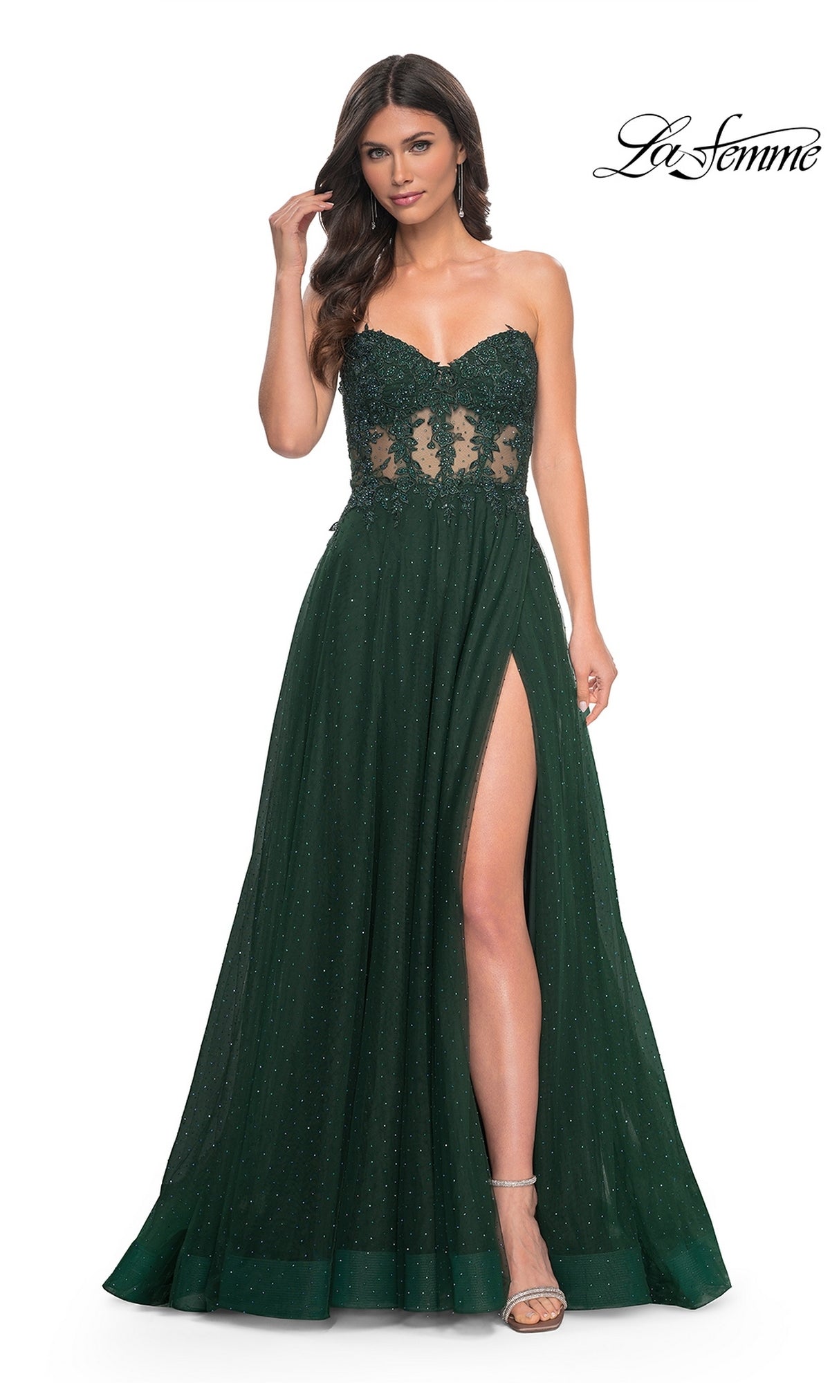 A woman models the La Femme Sheer-Waist Long A-Line Prom Dress 32313, a strapless dark green gown with a beaded lace bodice, sheer waist detailing, and a high leg slit, standing before a plain white background.