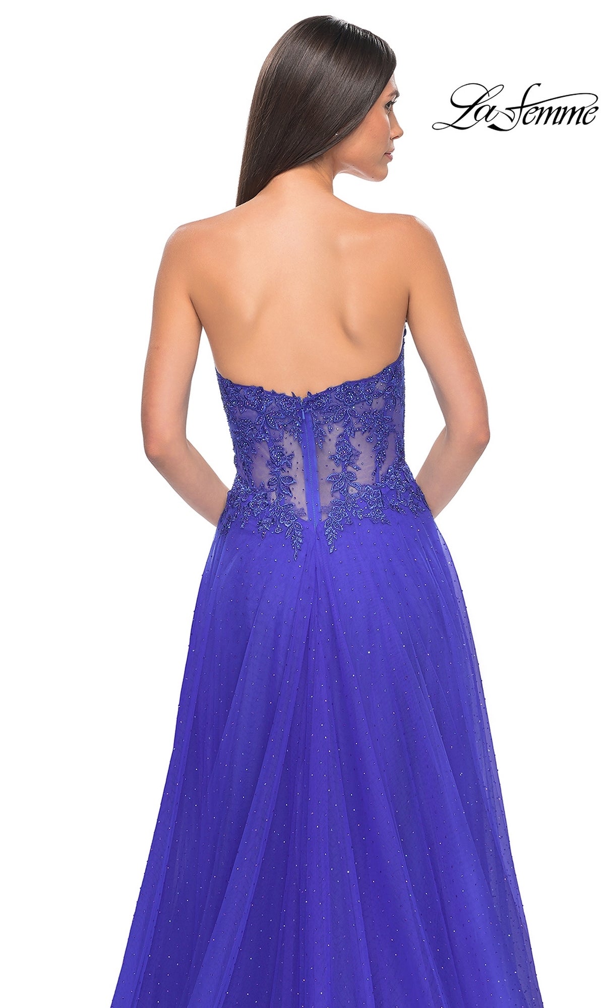 A woman faces away from the camera in the La Femme Sheer-Waist Long A-Line Prom Dress 32313, featuring a strapless royal blue design with a beaded lace bodice and floor-length shimmer overlay.