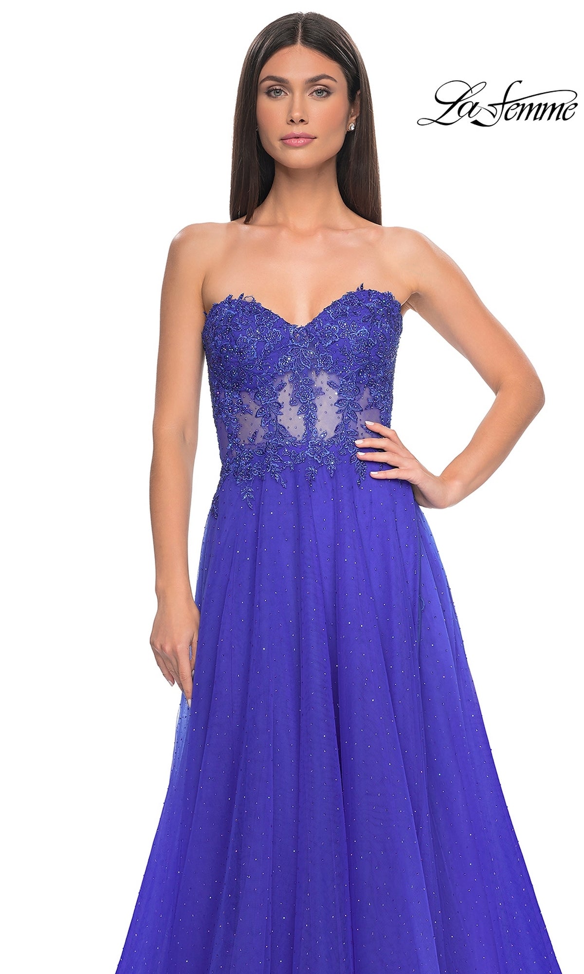 A woman wearing the La Femme Sheer-Waist Long A-Line Prom Dress 32313 in royal blue, featuring a beaded lace bodice with sheer detailing and subtle shimmer overlay, stands against a white background. 