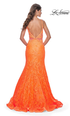 A woman stands with her back to the camera, showcasing the La Femme Bright Long Lace Mermaid Prom Dress 32314 in orange, featuring a low back and spaghetti straps.
