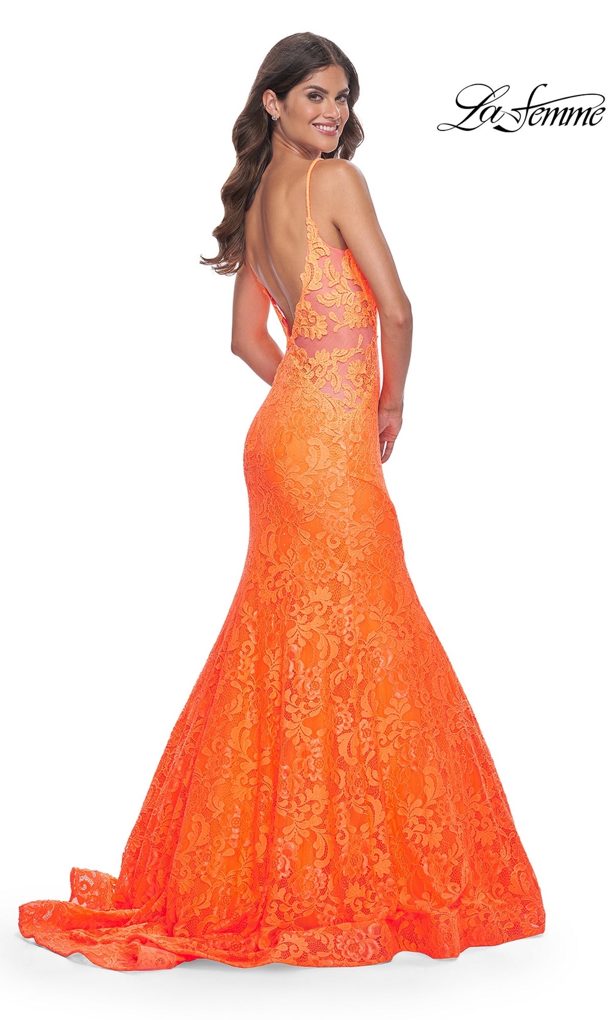A woman poses and smiles over her shoulder in the La Femme Bright Long Lace Mermaid Prom Dress 32314, featuring a low back, delicate spaghetti straps, floor-length train, and vibrant orange lace.