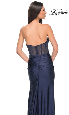 Woman in a strapless navy blue La Femme Strapless Beaded Long Prom Dress 32316, featuring a sheer back panel and rhinestone embellishments, stands with her back to the camera.