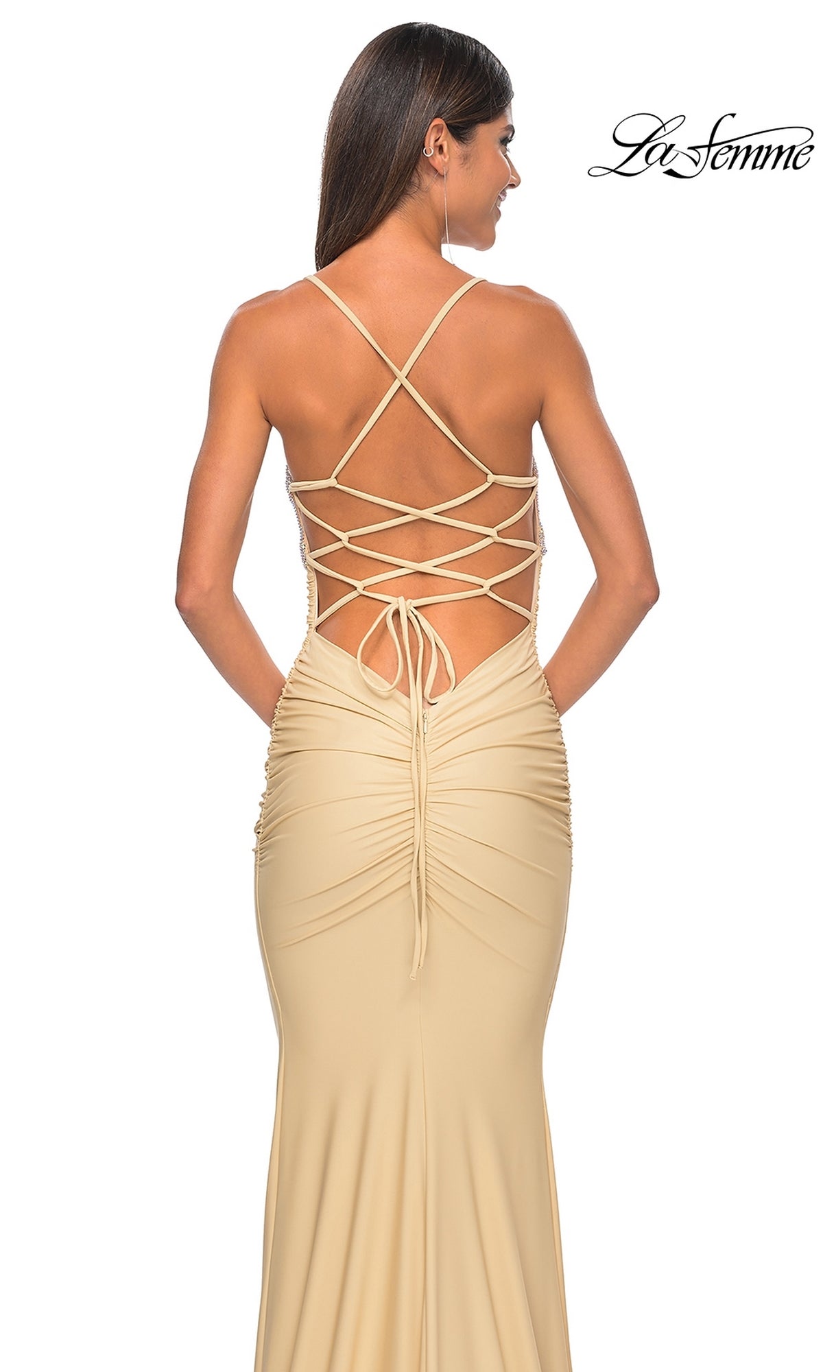 A woman is seen from behind wearing the La Femme Embellished-Bodice Long Prom Dress 32320 in beige, featuring crisscross lace-up straps and ruched details. The 