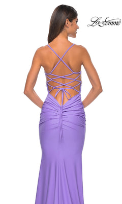 A woman stands with her back to the camera wearing the La Femme Embellished-Bodice Long Prom Dress 32320, featuring a lavender hue, backless design, crisscross lace-up detail, and ruched sides.
