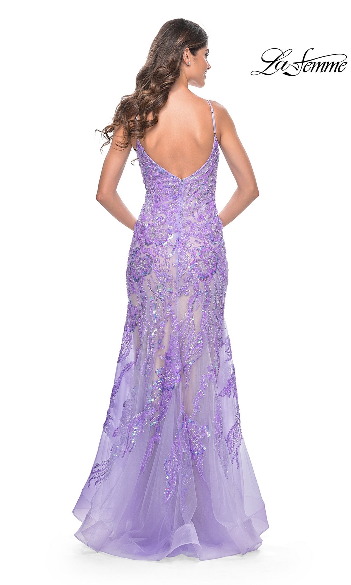 A woman in a fitted lavender Le Femme Long Sequin-Lace Prom Dress 32333, featuring a low back and spaghetti straps, stands facing away from the camera, highlighting the elegance of this mermaid formal gown.