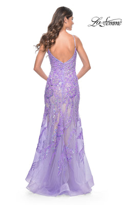 A woman in a fitted lavender Le Femme Long Sequin-Lace Prom Dress 32333, featuring a low back and spaghetti straps, stands facing away from the camera, highlighting the elegance of this mermaid formal gown.