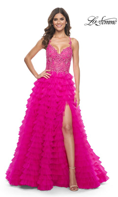 A woman stands smiling in the La Femme Hot Pink Long Ruffled Prom Dress 32334, featuring an embroidered-lace bodice, thin straps, and a high-slit ruffled A-line skirt.
