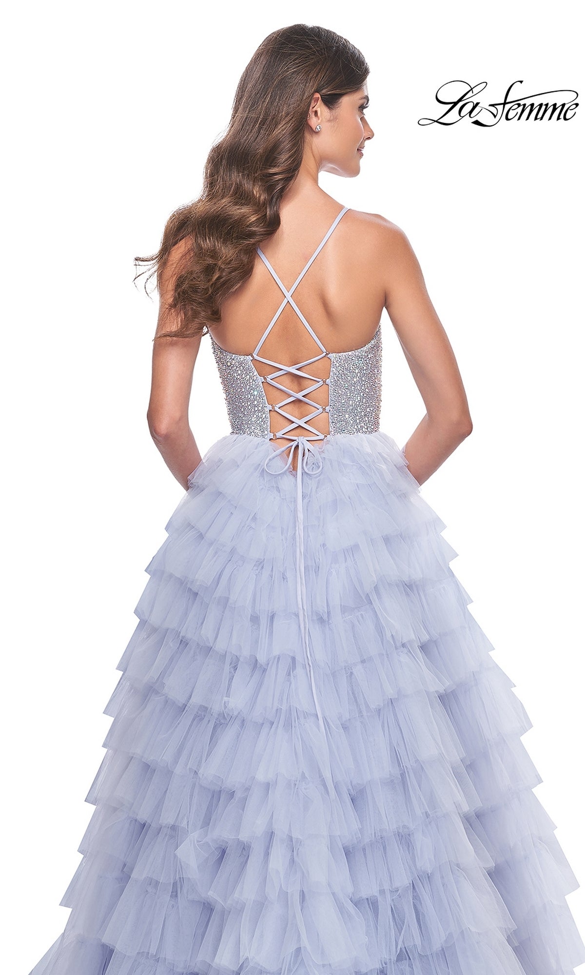 A woman is shown from behind wearing the La Femme Long Tiered A-Line Prom Dress 32335, featuring a beaded sweetheart corset, crisscross lace-up back, and sparkly bodice, set against a white background.