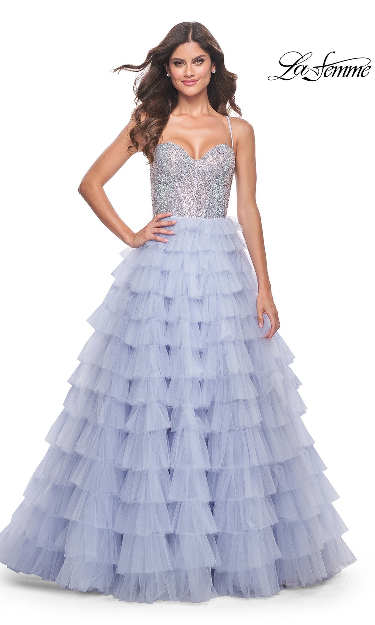 A woman smiles against a white background, wearing the La Femme Long Tiered A-Line Prom Dress 32335 with a sleeveless silver beaded sweetheart corset and a layered lavender tulle skirt featuring a thigh-high side slit.