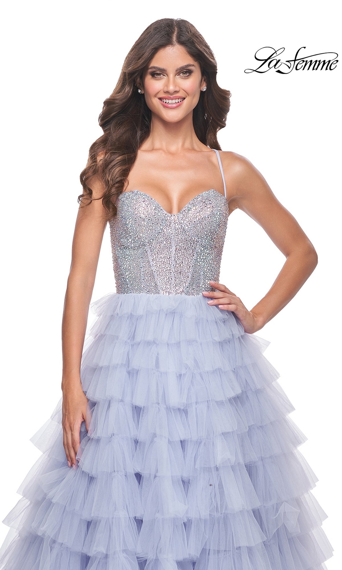 A woman poses and smiles against a white background wearing the La Femme Long Tiered A-Line Prom Dress 32335, featuring a sparkly silver beaded sweetheart corset top and long purple tulle skirt. The 