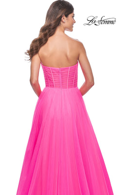 A woman models the La Femme Long Pink Corset A-Line Prom Dress 32341, a strapless neon pink gown with a fitted corset-style bodice and floor-length skirt, shown from the back.