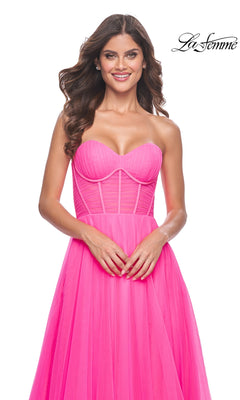 A woman wears the La Femme Long Pink Corset A-Line Prom Dress 32341, a strapless neon pink gown featuring a fitted corset-style bodice, shown against a white background.