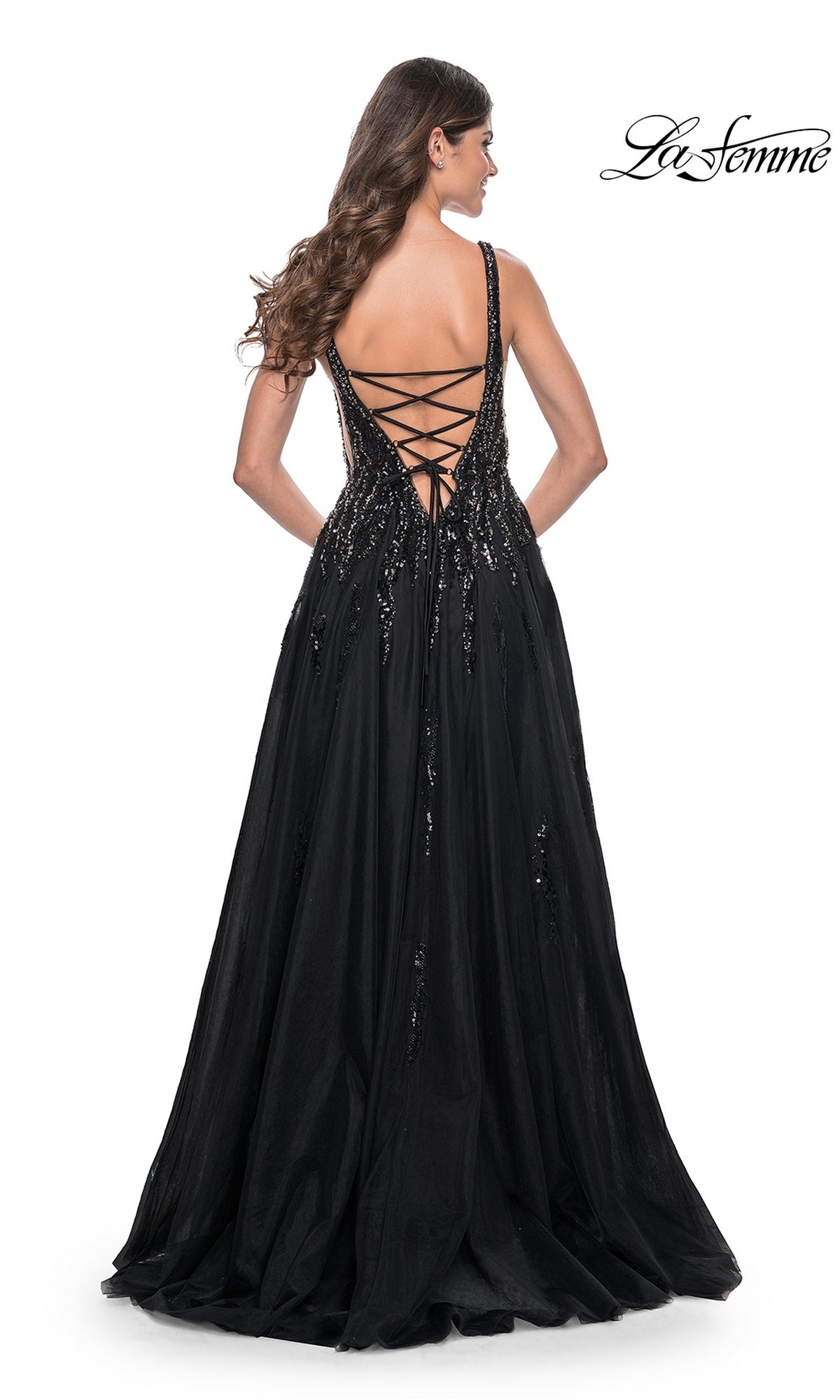 Woman models the La Femme Deep V-Neck Long Black Prom Dress 32345, featuring sequin details and a lace-up open back, while standing and facing away from the camera.