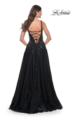 Woman models the La Femme Deep V-Neck Long Black Prom Dress 32345, featuring sequin details and a lace-up open back, while standing and facing away from the camera.