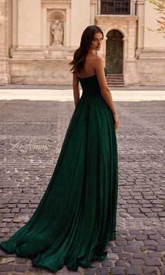 A woman wears the La Femme 32382 strapless long metallic prom dress, standing on a cobblestone street and glancing over her shoulder, with a historic stone building in the background.