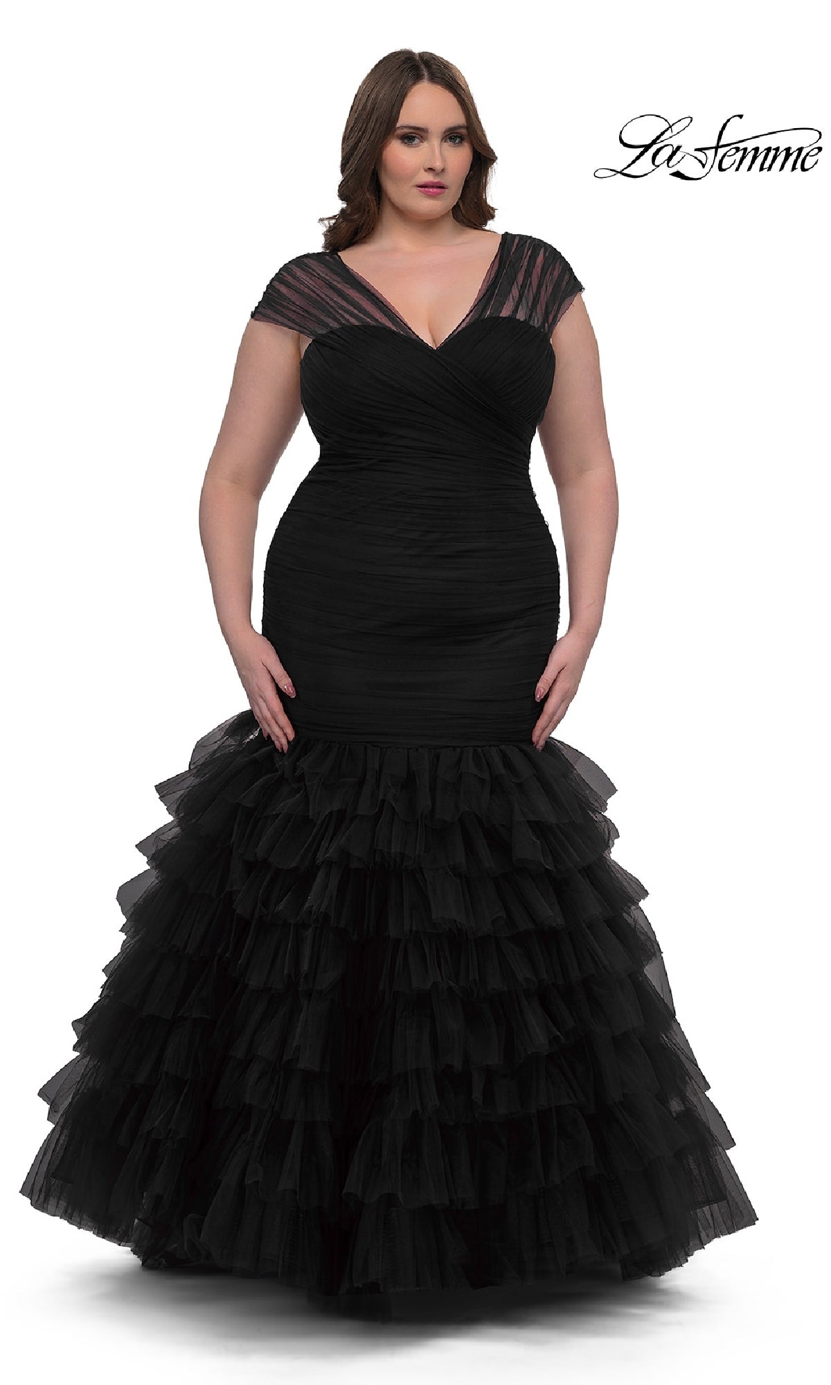 A woman models the Plus-Size Long Mermaid Prom Dress: La Femme 32389, featuring a black fitted silhouette with layered tulle ruffles and a sweetheart corset bodice, against a white background. The La Femme logo appears in the top right corner.