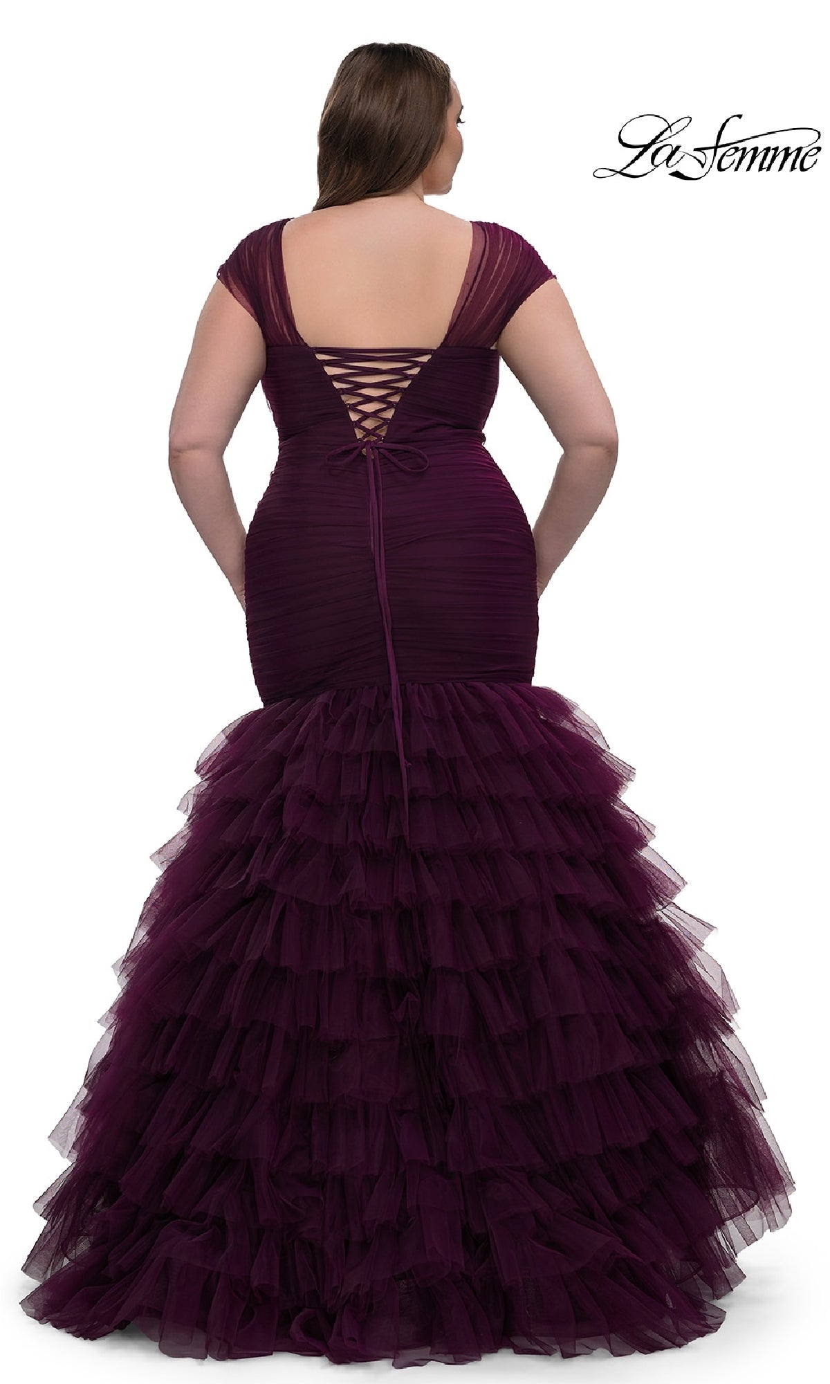 A woman wearing the La Femme 32389 plus-size long mermaid prom dress in deep purple with a ruffled tulle skirt and lace-up open back, standing and facing away from the camera.