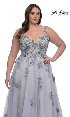 A woman models the La Femme 32412 long plus-size prom ball gown in light purple with blue floral lace, sheer details, and a corset bodice, standing against a white background.