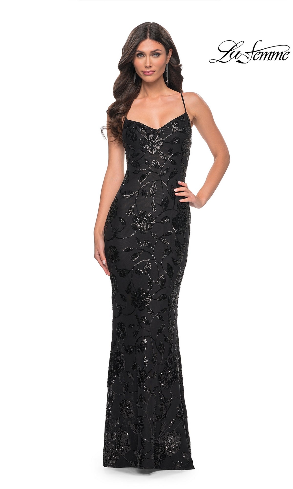 A woman models the Long Black Sequin-Print Prom Dress: La Femme 32415, featuring floral patterns and thin straps, standing against a plain white background with the 