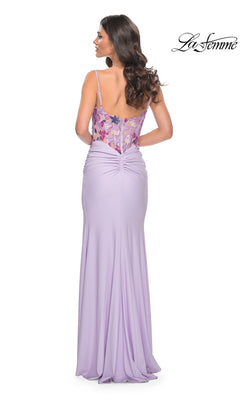 Seen from the back with long wavy hair, a woman wears the La Femme 32419: a light periwinkle, floor-length prom dress featuring floral embroidery on its fitted corset-style bodice. The La Femme logo appears in the top right corner.